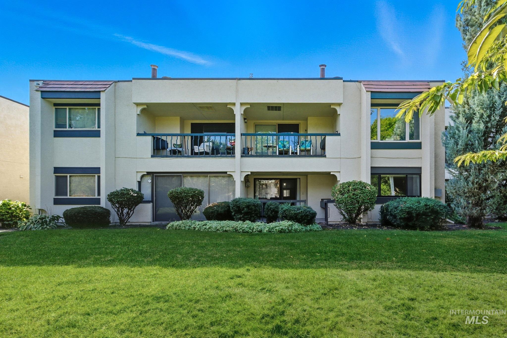 Rear view of property featuring stucco siding, a yard, and a balcony