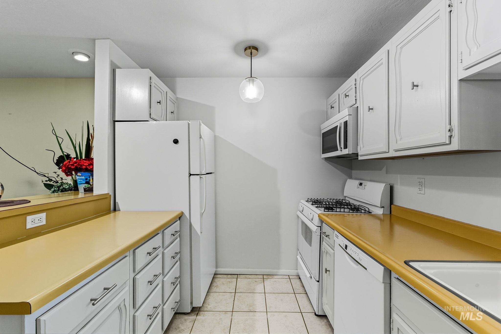 Kitchen featuring pendant lighting, white appliances, light countertops, and white cabinetry