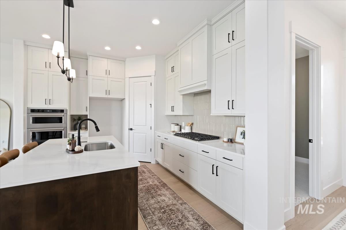 Kitchen with hanging light fixtures, an island with sink, white cabinetry, recessed lighting, and light stone counters