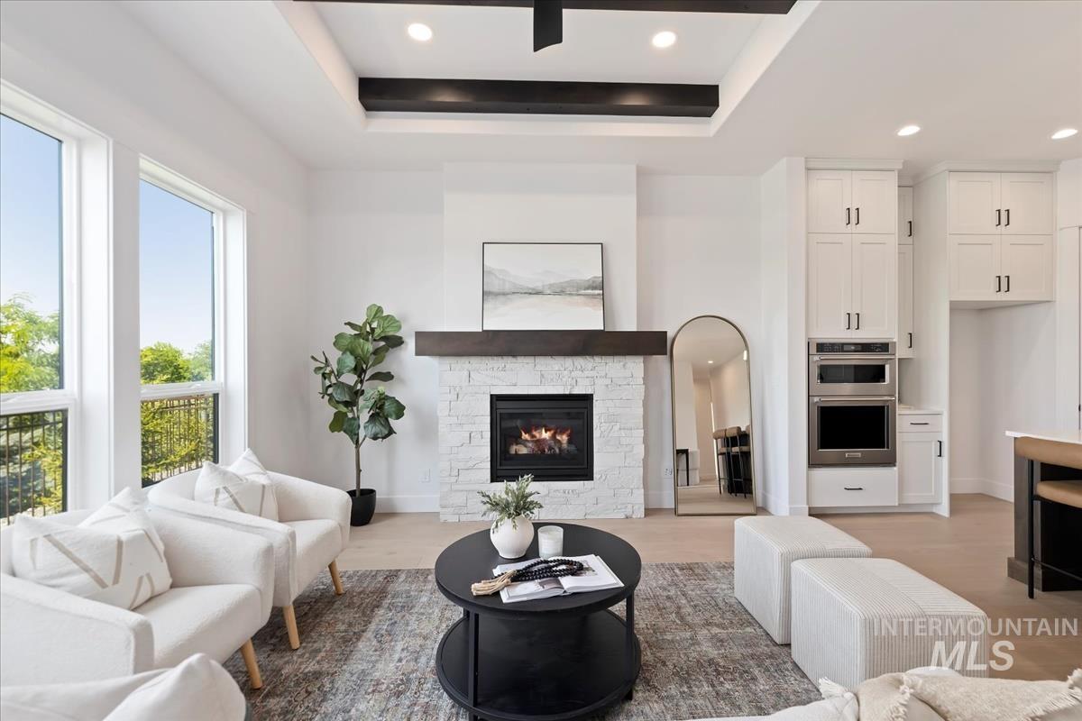 Living room with a fireplace, recessed lighting, light wood-style flooring, and a tray ceiling