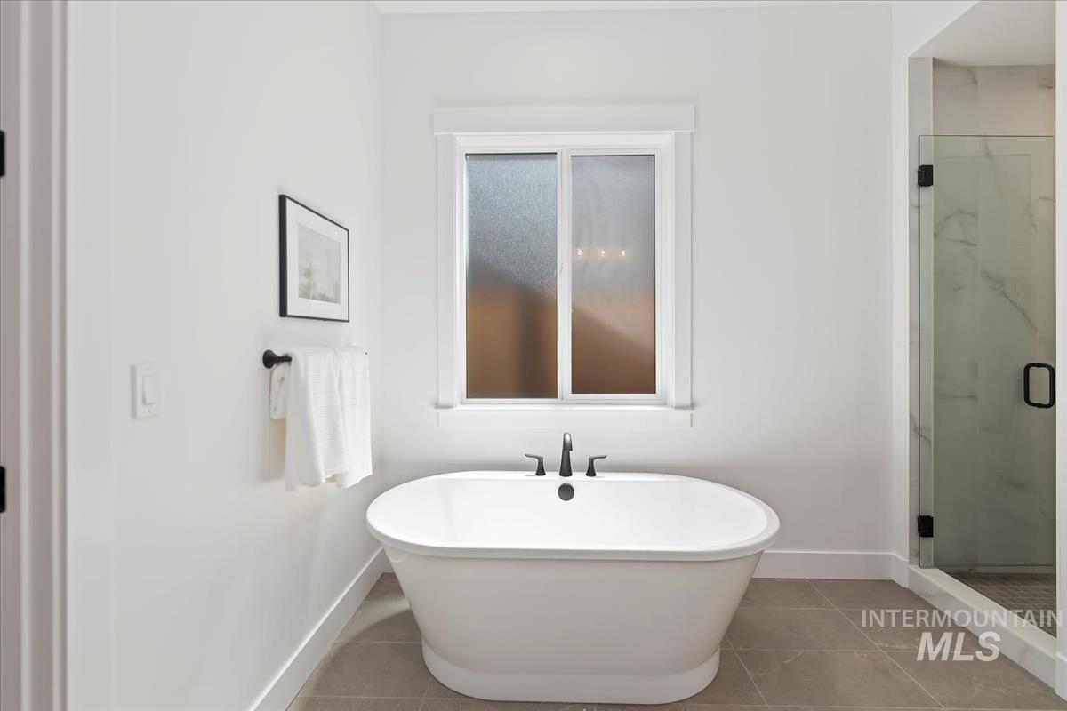 Bathroom featuring a freestanding tub, a marble finish shower, and tile patterned flooring