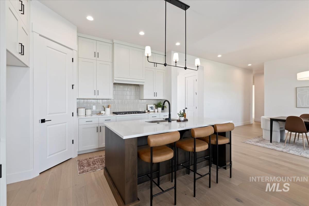 Kitchen with white cabinetry, a breakfast bar area, pendant lighting, a center island with sink, and light wood-style flooring