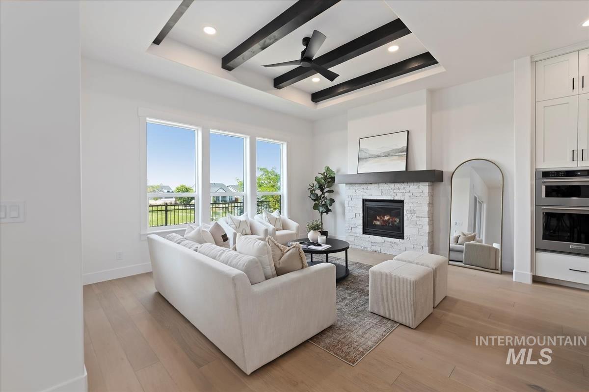 Living area with a stone fireplace, light wood finished floors, a ceiling fan, recessed lighting, and a tray ceiling