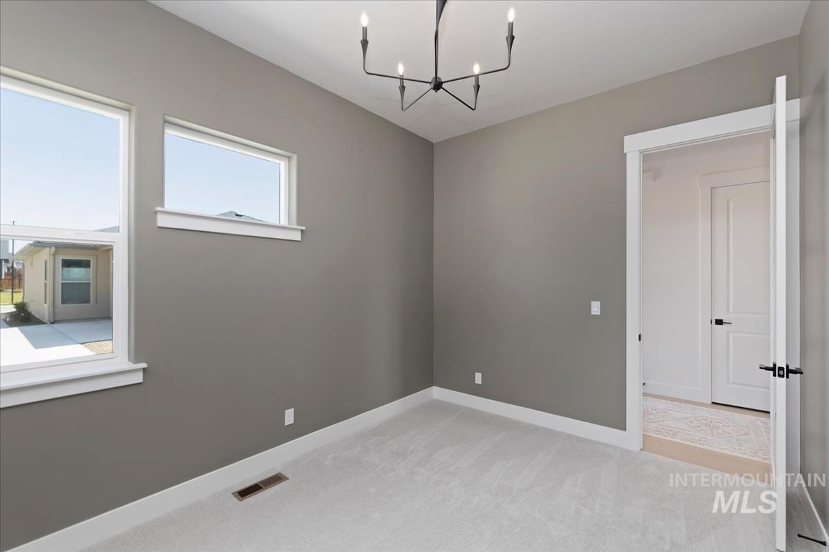 Empty room with light colored carpet and a chandelier