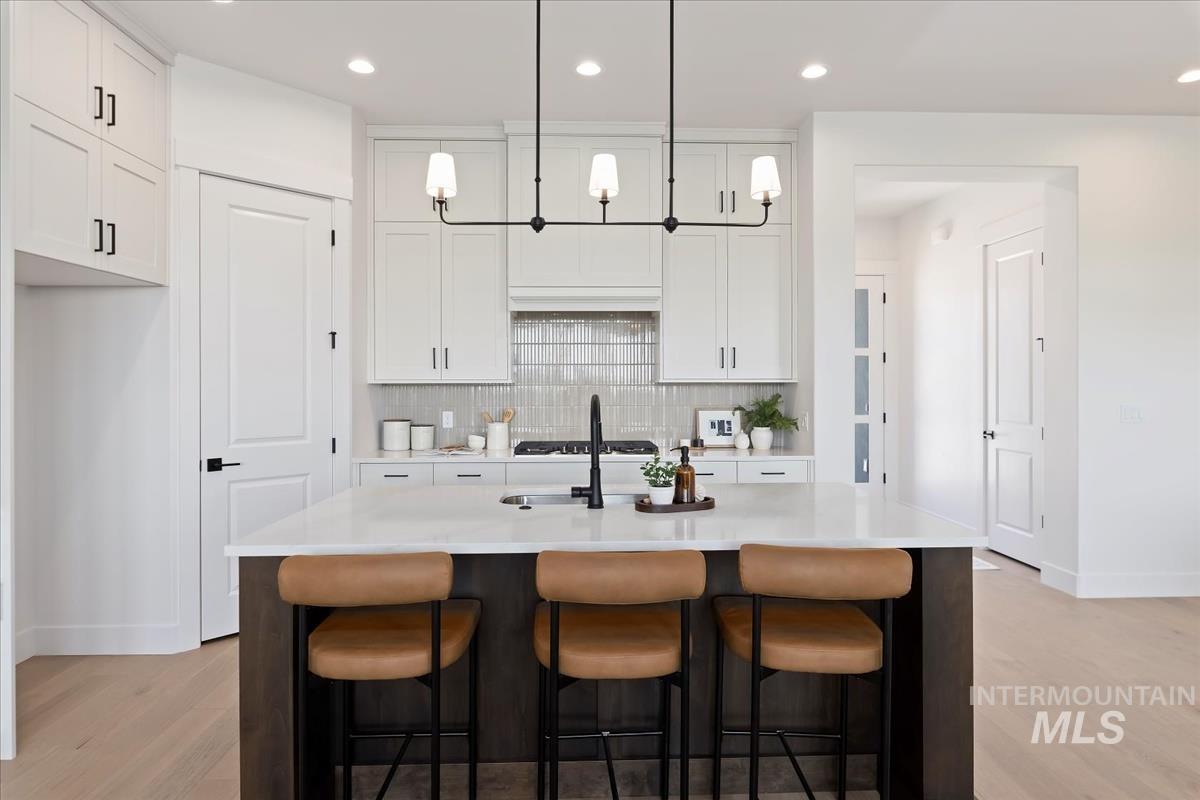 Kitchen with hanging light fixtures, backsplash, a kitchen bar, white cabinetry, and recessed lighting