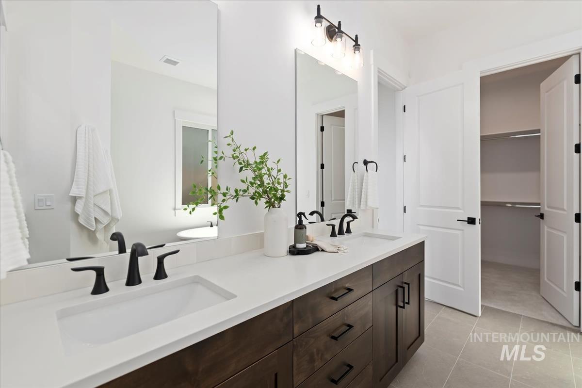 Full bathroom with double vanity, light tile patterned floors, and a walk in closet
