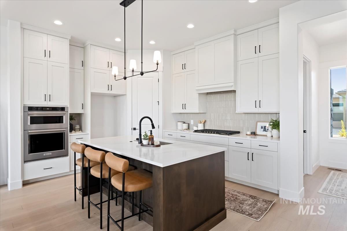 Kitchen featuring dark brown cabinets, a center island with sink, a breakfast bar, white cabinetry, and decorative light fixtures