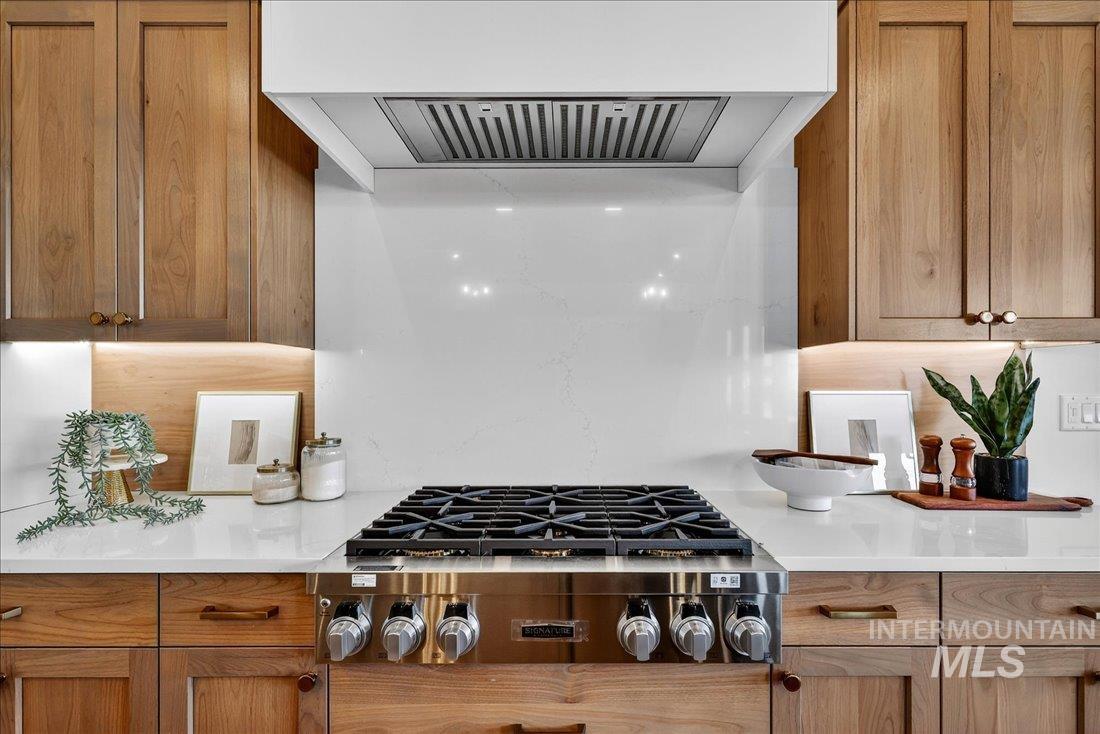 Kitchen featuring exhaust hood, stainless steel gas cooktop, light stone countertops, and brown cabinets