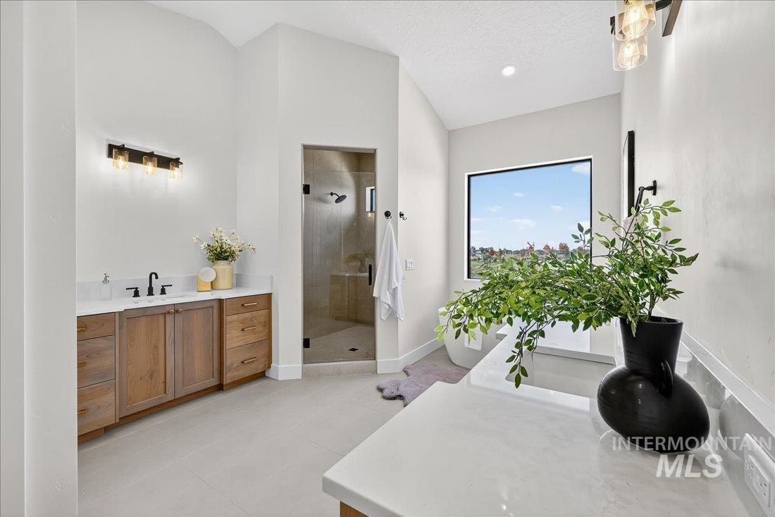 Full bath featuring vanity, a shower stall, light tile patterned floors, lofted ceiling, and a freestanding tub