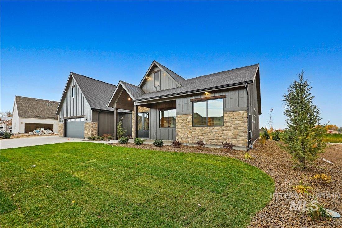 Modern farmhouse style home featuring stone siding, board and batten siding, a front yard, covered porch, and driveway