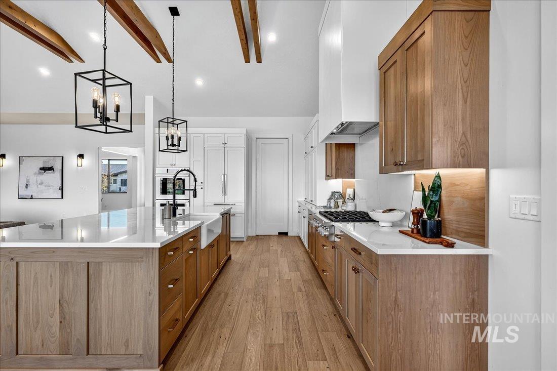 Kitchen featuring brown cabinetry, light wood finished floors, a spacious island, decorative light fixtures, and light stone counters