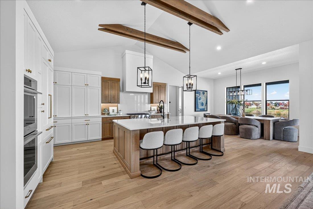 Kitchen with beamed ceiling, a kitchen bar, decorative light fixtures, a kitchen island with sink, and light wood-type flooring