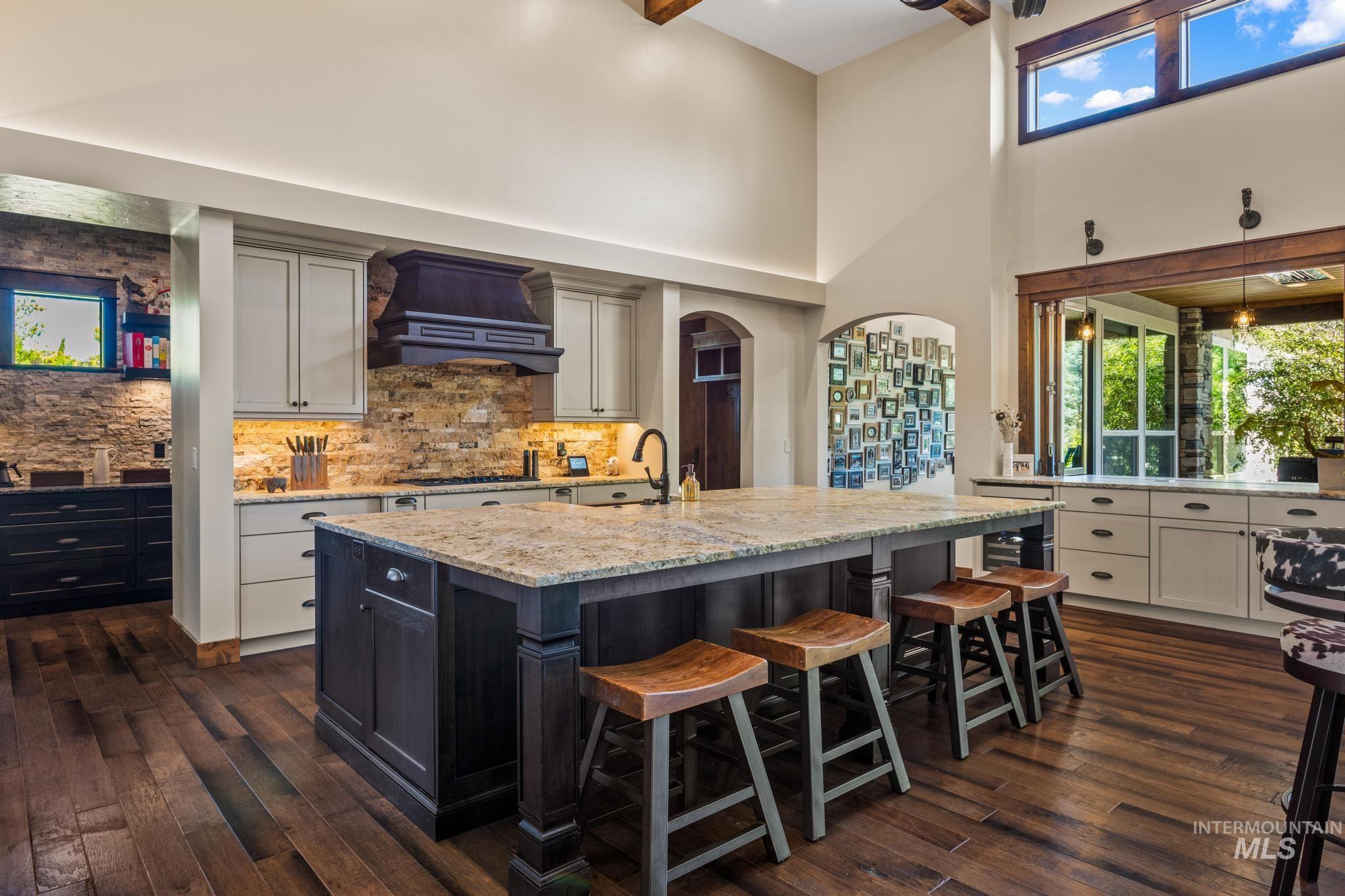 Kitchen featuring dark wood-style flooring, backsplash, a high ceiling, an island with sink, and a breakfast bar area