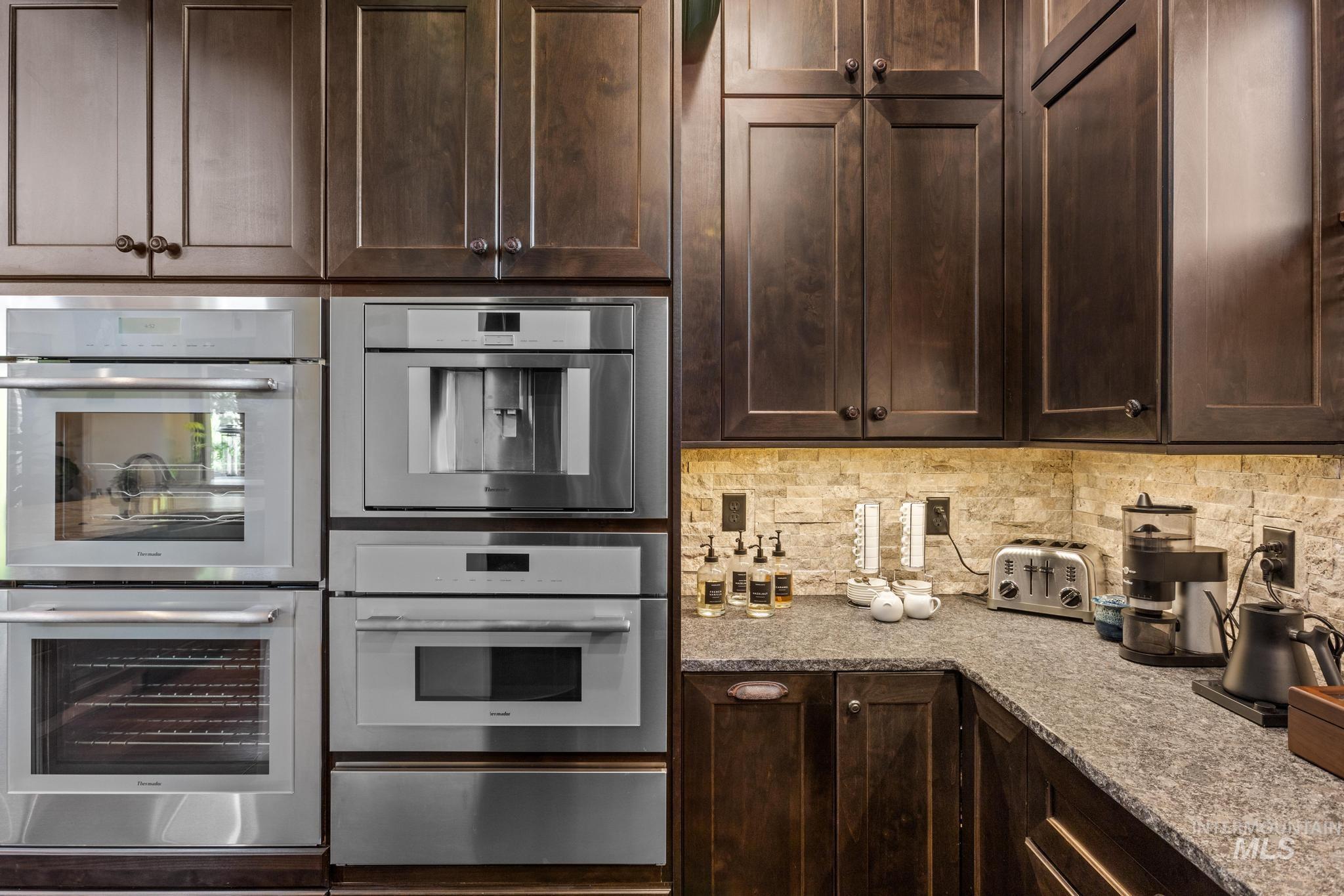 Kitchen with double oven, white double oven, a warming drawer, dark brown cabinets, and backsplash