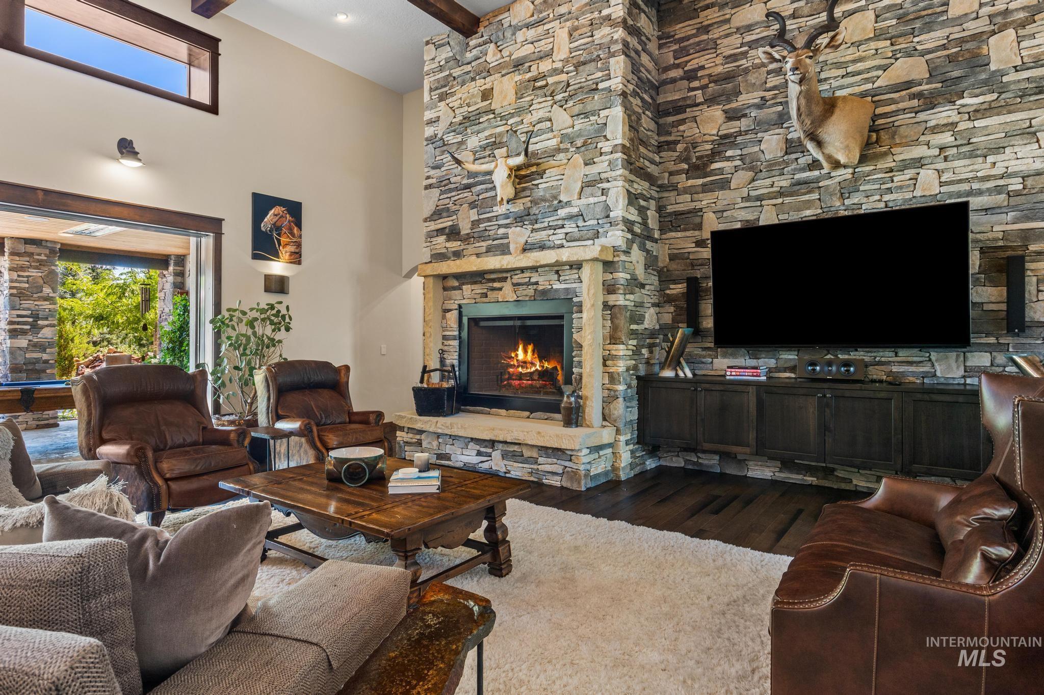 Living room with a stone fireplace, dark wood-style flooring, beam ceiling, and a towering ceiling