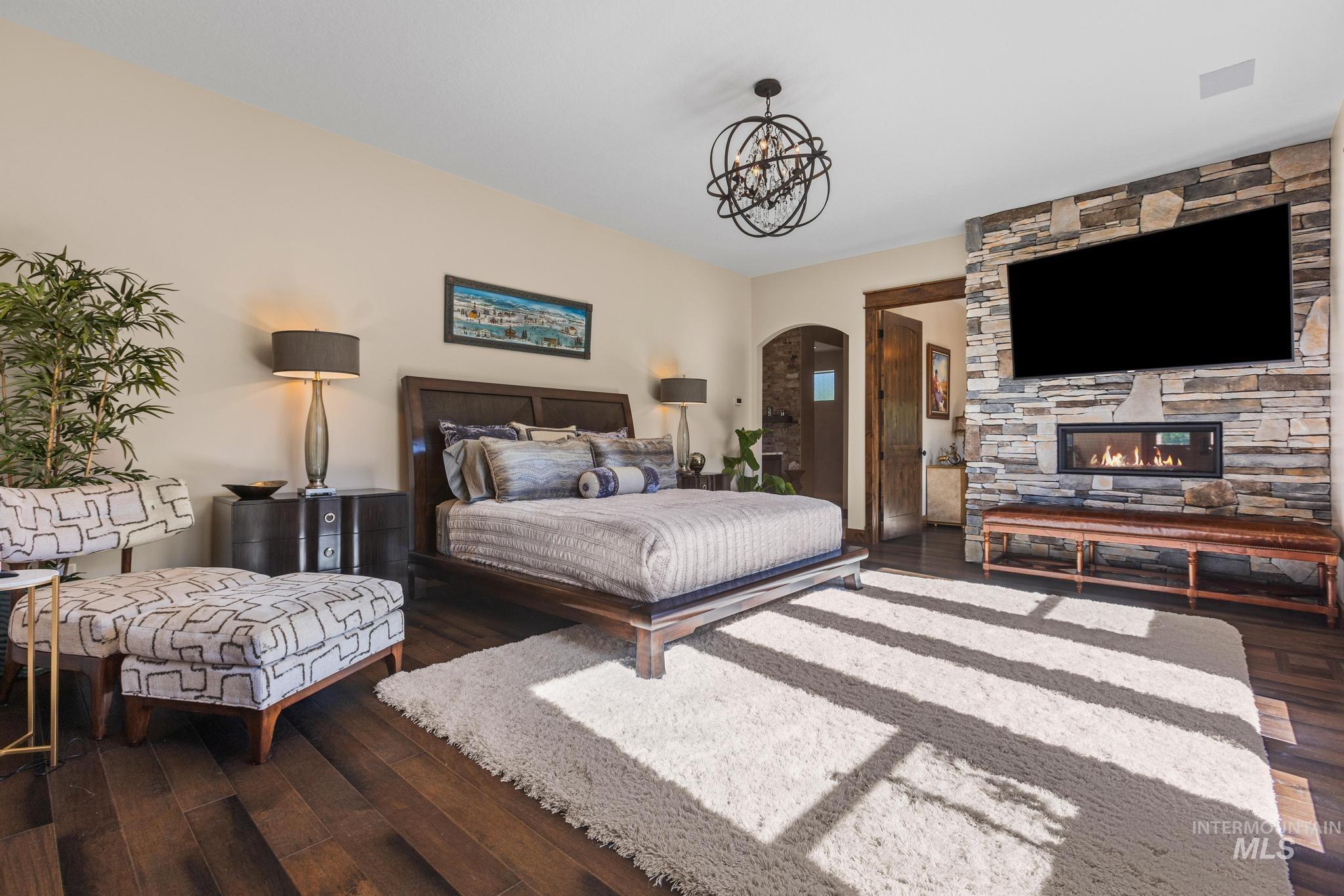Bedroom featuring arched walkways, wood finished floors, a chandelier, and a stone fireplace