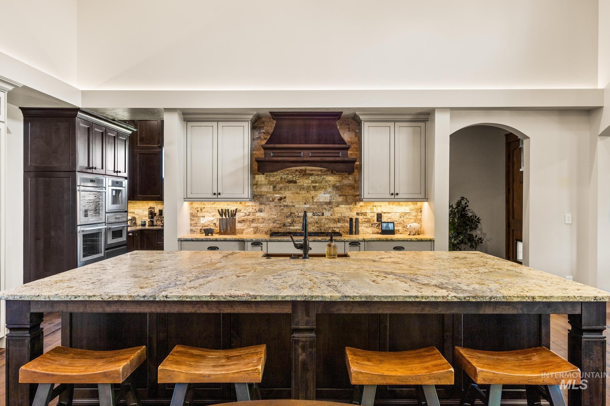 Kitchen with light stone counters, tasteful backsplash, arched walkways, and double oven