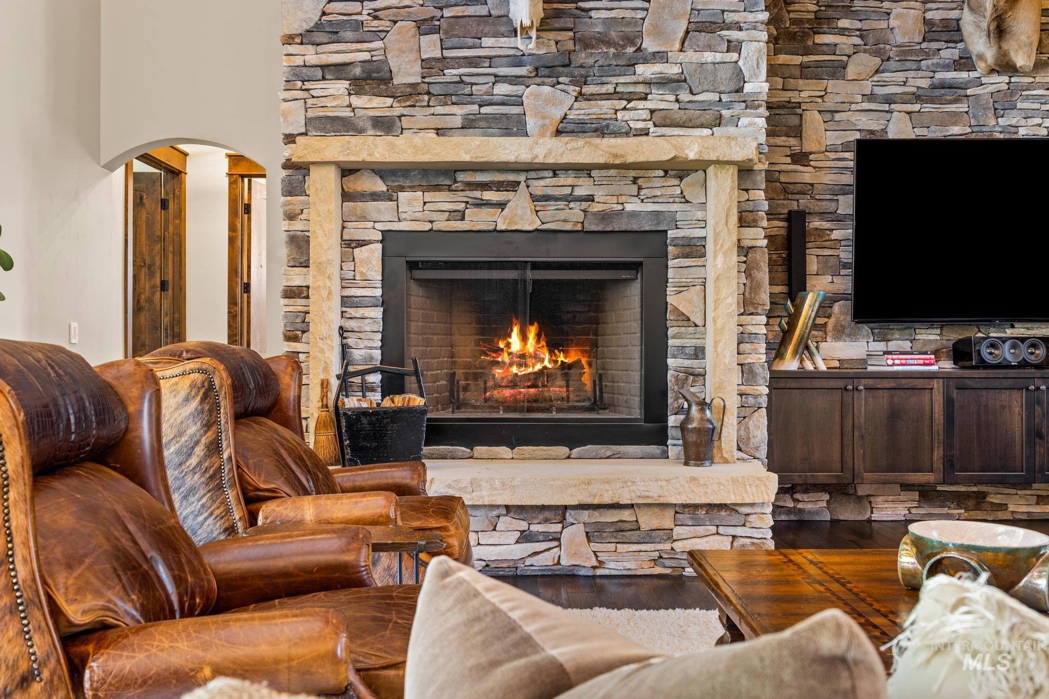 Living area featuring arched walkways, a stone fireplace, and wood finished floors