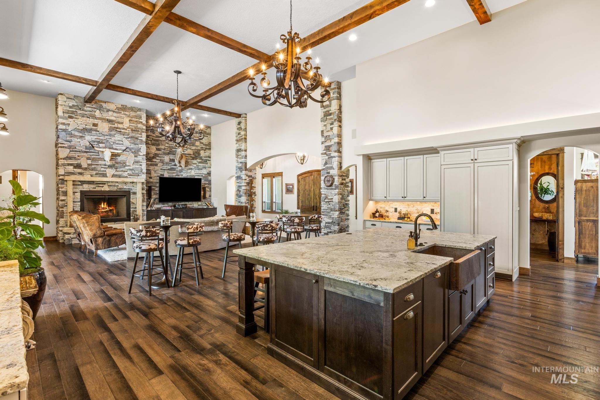 Kitchen with arched walkways, beam ceiling, a fireplace, light stone counters, and dark wood-type flooring