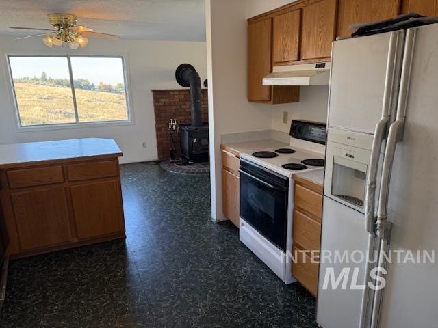 Kitchen featuring white appliances, a wood stove, brown cabinetry, light countertops, and under cabinet range hood