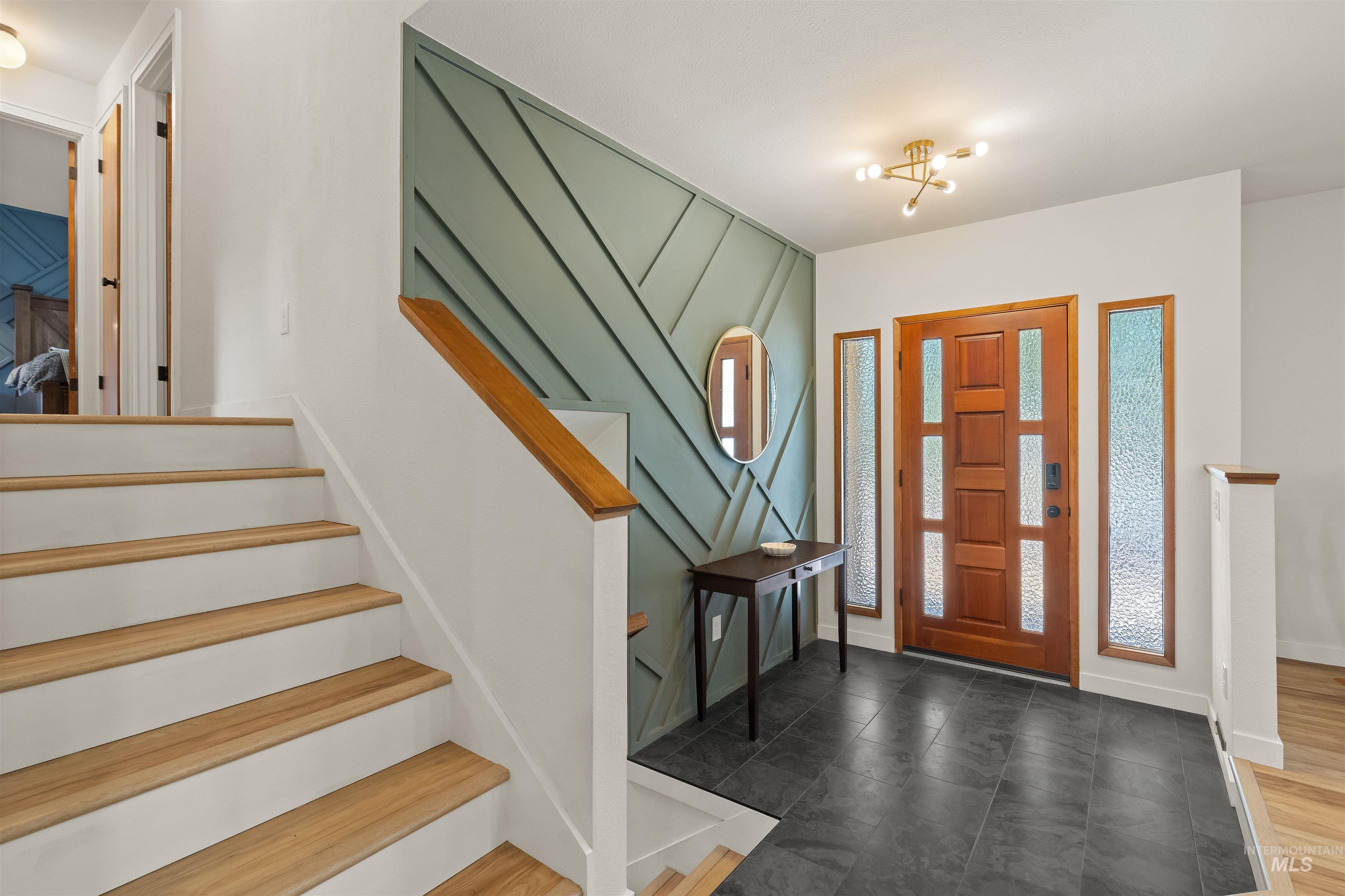 Entryway featuring a wood-panel accent wall, rich wood-finish front door with privacy glass sidelights, and dark tile flooring