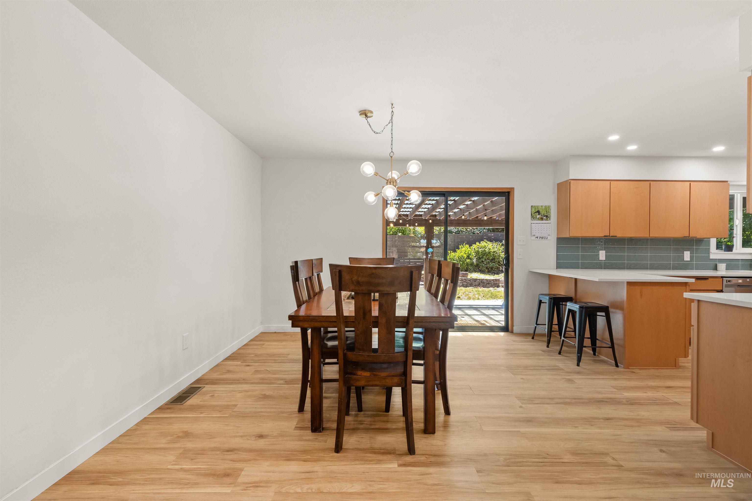 Open-concept dining area with wood-finish flooring, a modern chandelier, and a sliding glass door to the exterior