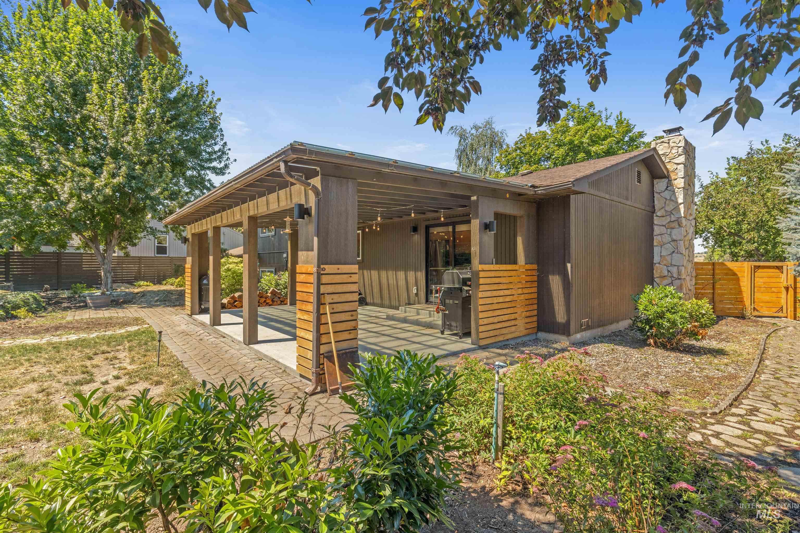 Expansive outdoor patio with a wooden pergola, stone-clad chimney, and horizontal slat wood accents
