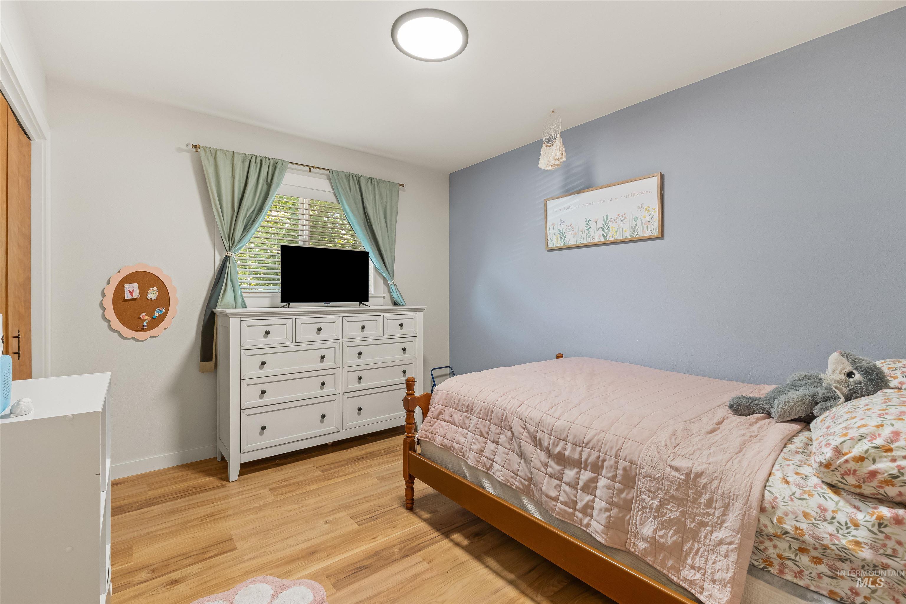Room featuring wood-finish flooring, a neutral wall color palette with an accent wall, window with blinds, and a flush-mount ceiling light fixture