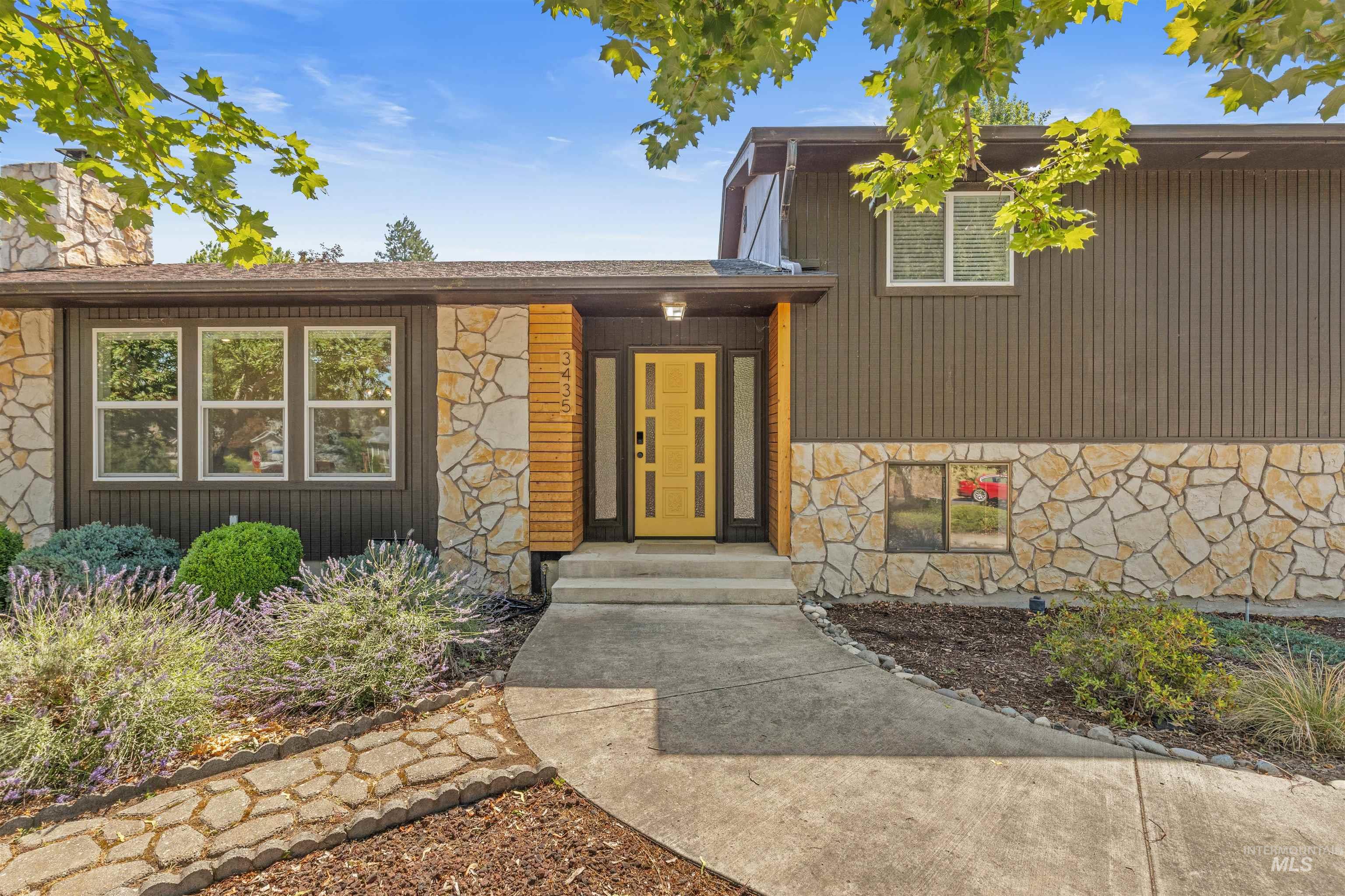 Exterior featuring a distinctive golden front door, natural stone veneer, textured vertical siding, and a concrete pathway