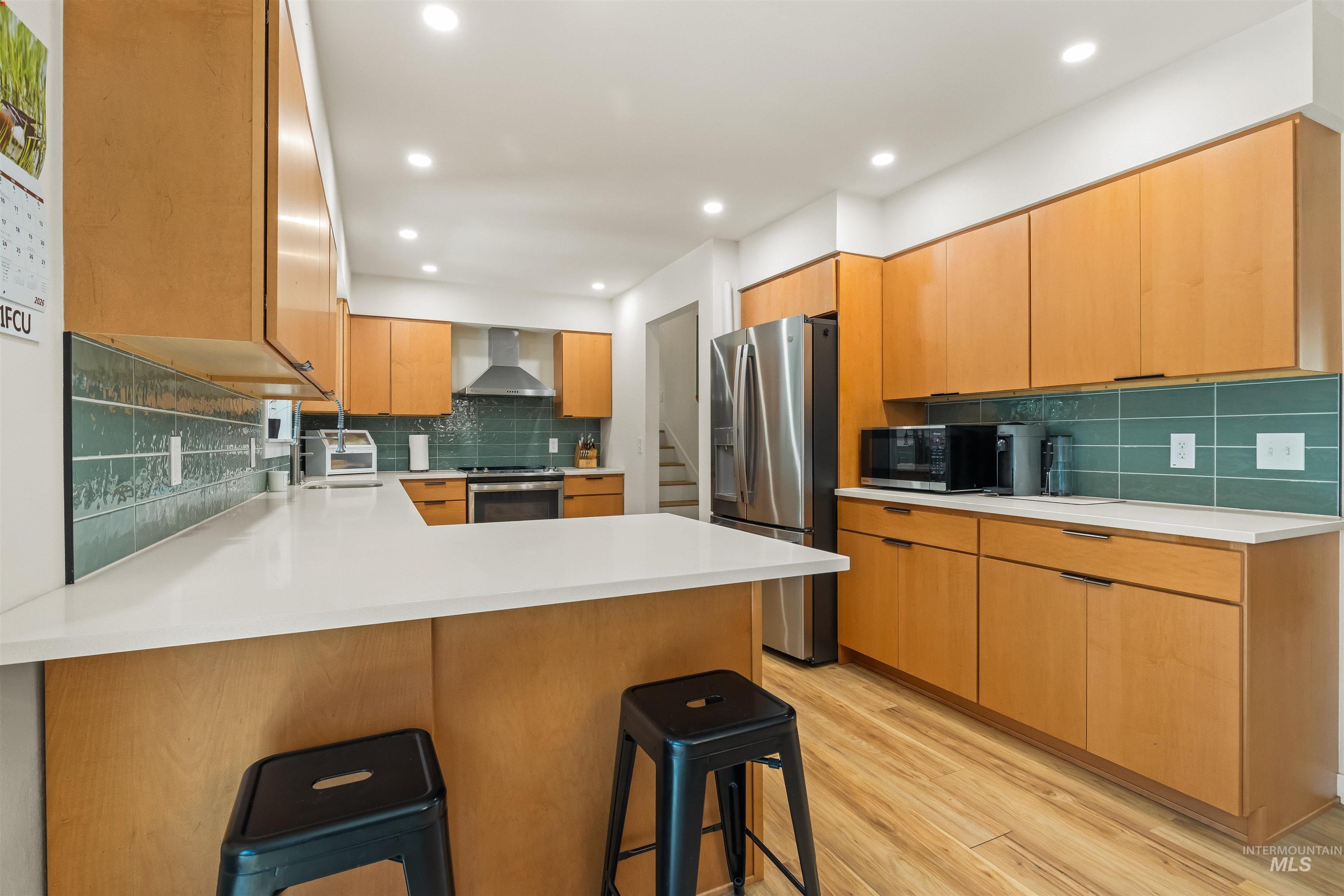 Well-appointed kitchen featuring light wood cabinetry, a large peninsula with a white countertop, and a teal subway tile backsplash