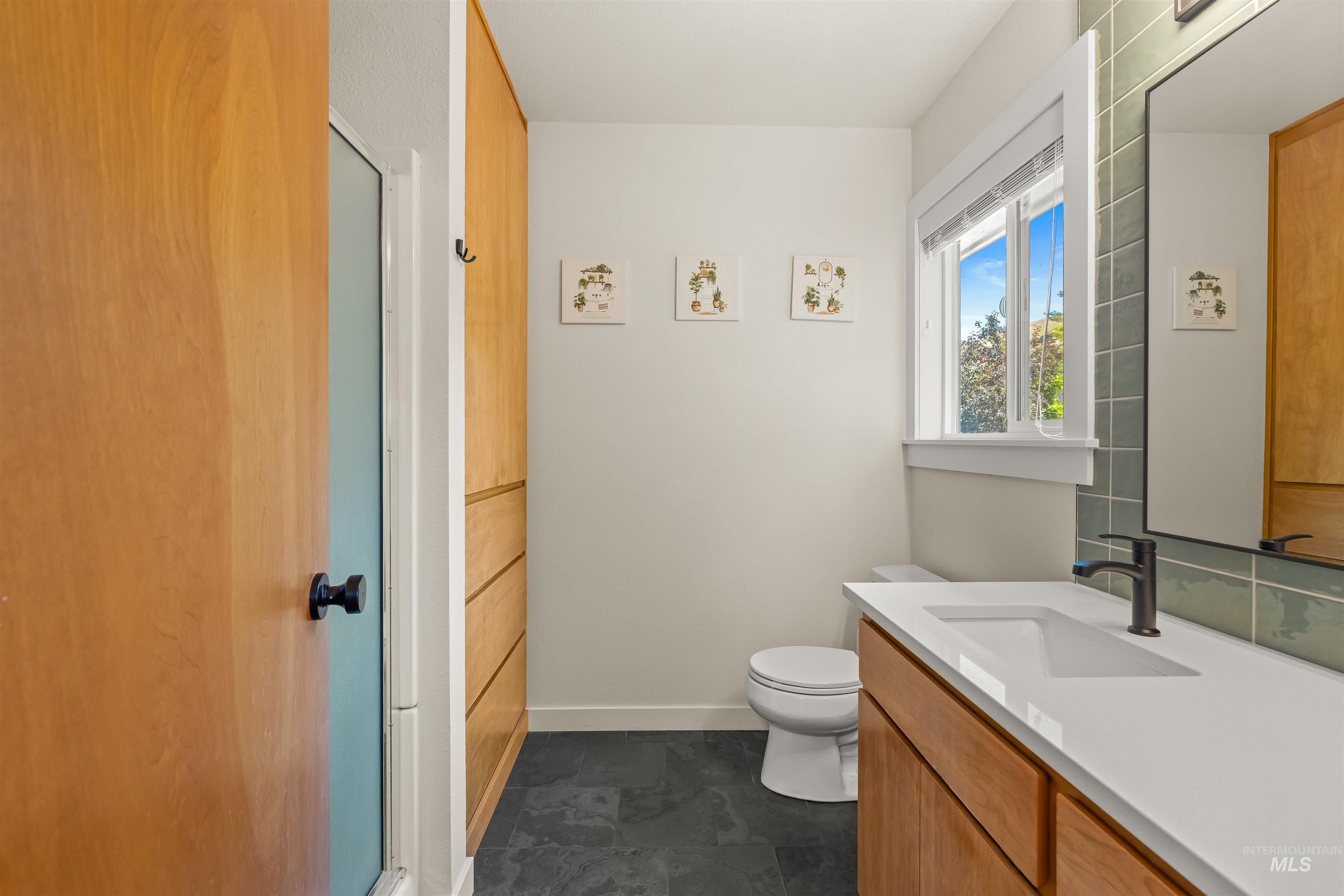 Bathroom featuring a wood-tone vanity with a white countertop and integrated sink, a rectangular mirror with a green tile surround, and a toilet