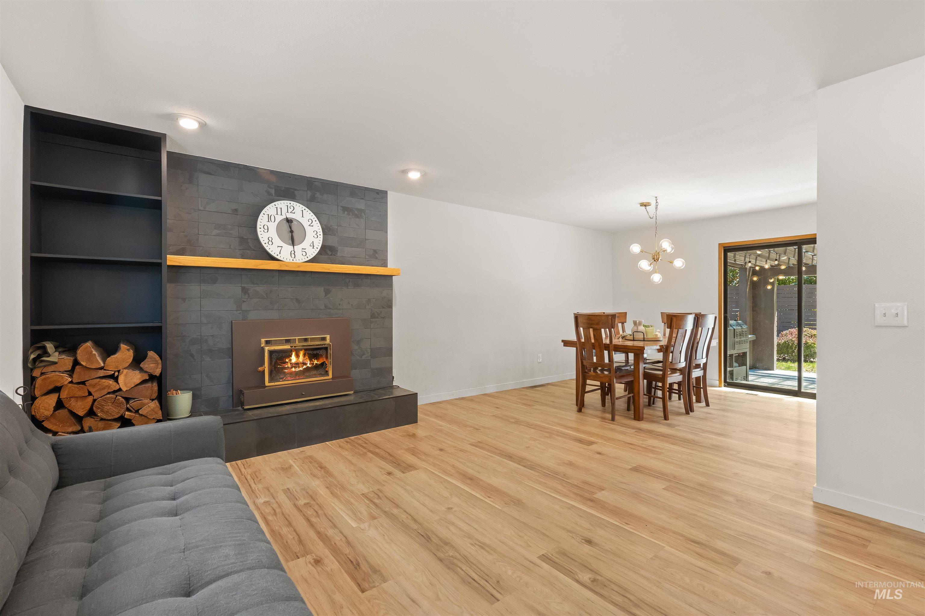 Open-concept living space featuring wood-finish flooring, a contemporary fireplace with a stone-tile surround, and a built-in shelving unit