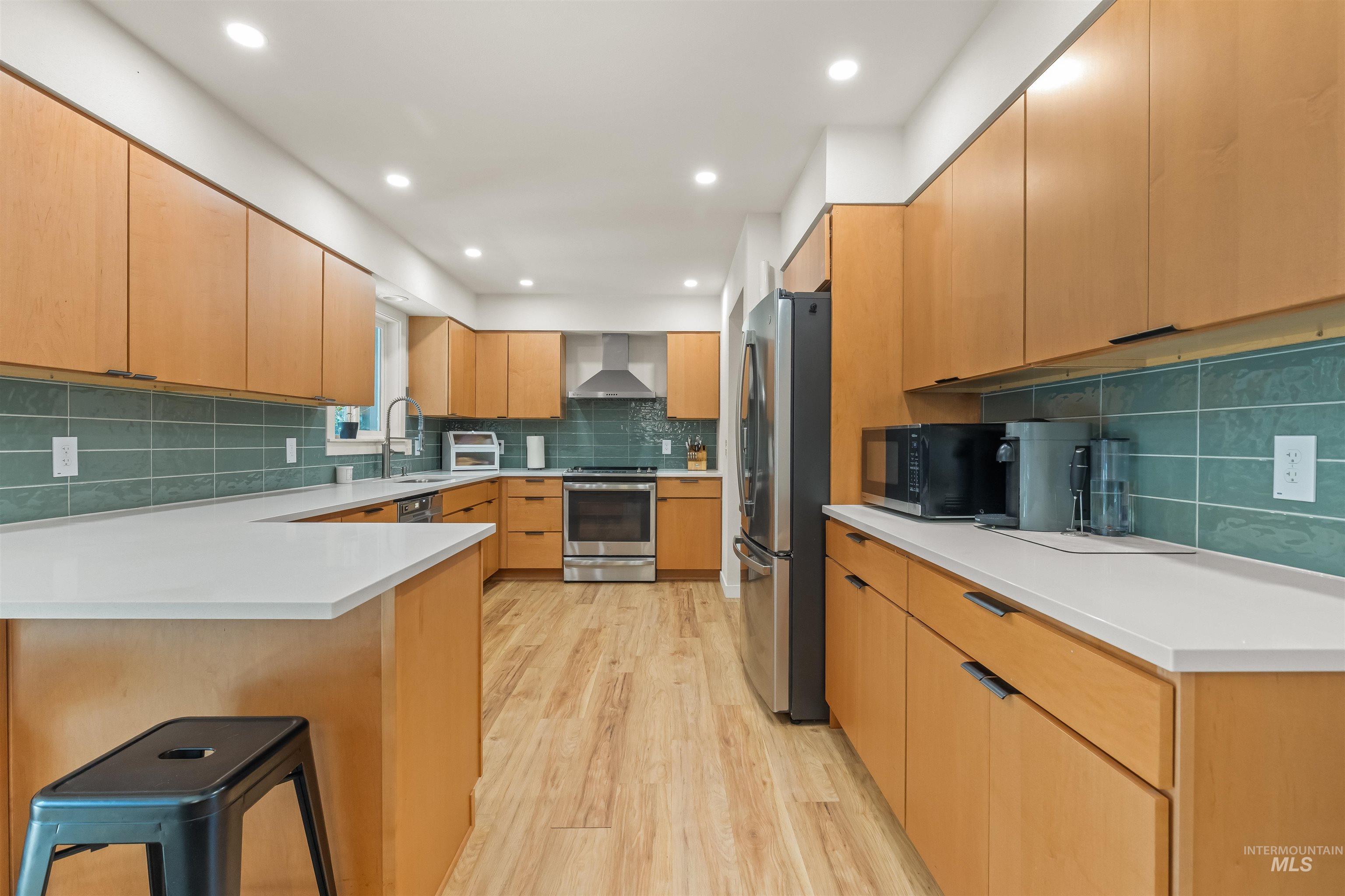 Kitchen with light wood-finish cabinetry, white countertops, and a teal subway tile backsplash