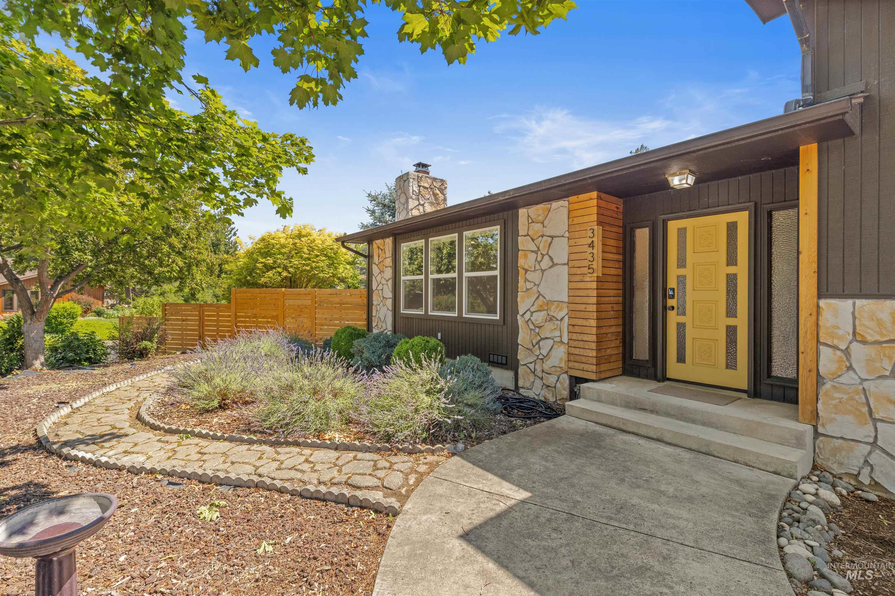 Contemporary exterior showcasing a bright yellow entry door with privacy glass sidelights, stonework accents, wood siding, and an established landscape with a stone pathway