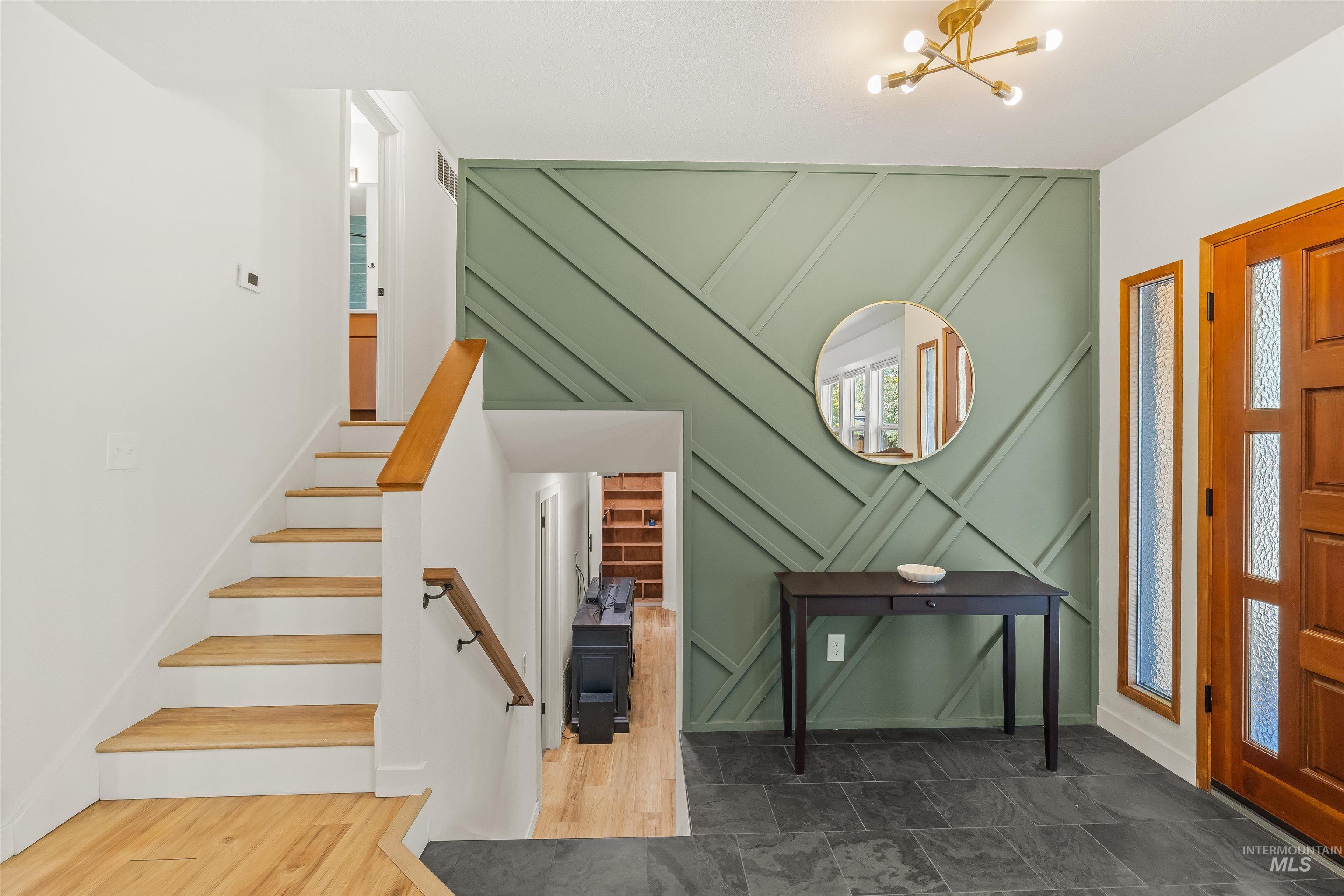 Entryway featuring a decorative accent wall with geometric paneling, slate tile flooring, and a natural wood staircase with a matching handrail