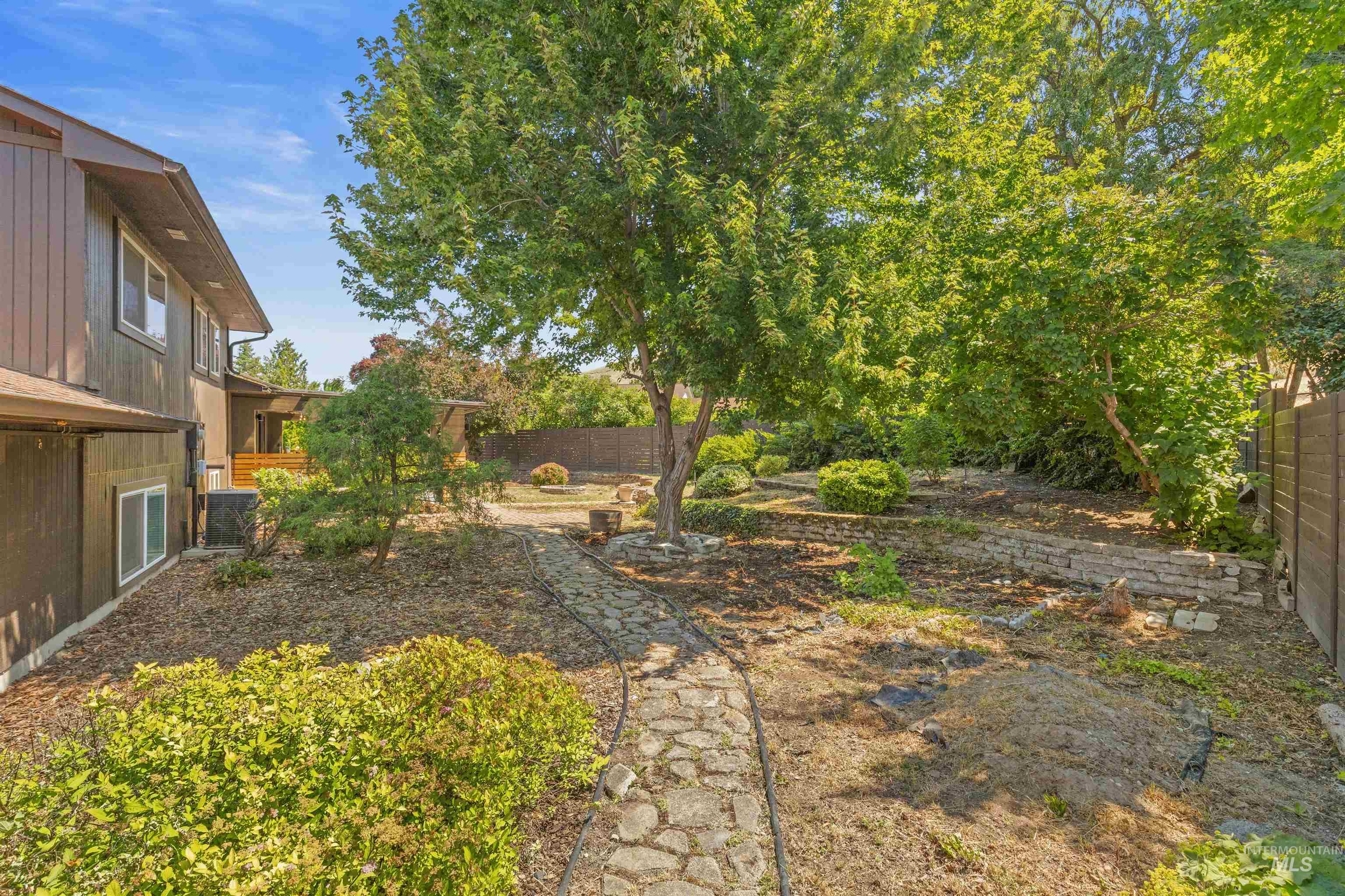 Tiered landscaping featuring mature trees, established shrubs, and a stone-paved pathway