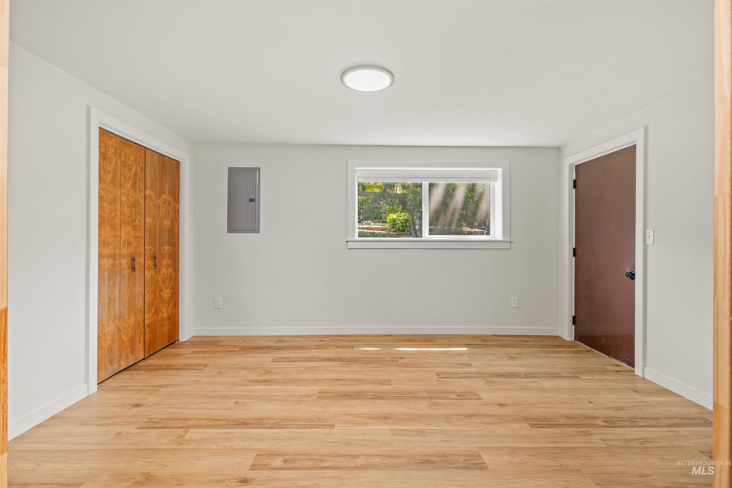 Spacious room featuring light wood-finish flooring, a flush-mount ceiling light, white walls, and a window providing natural illumination