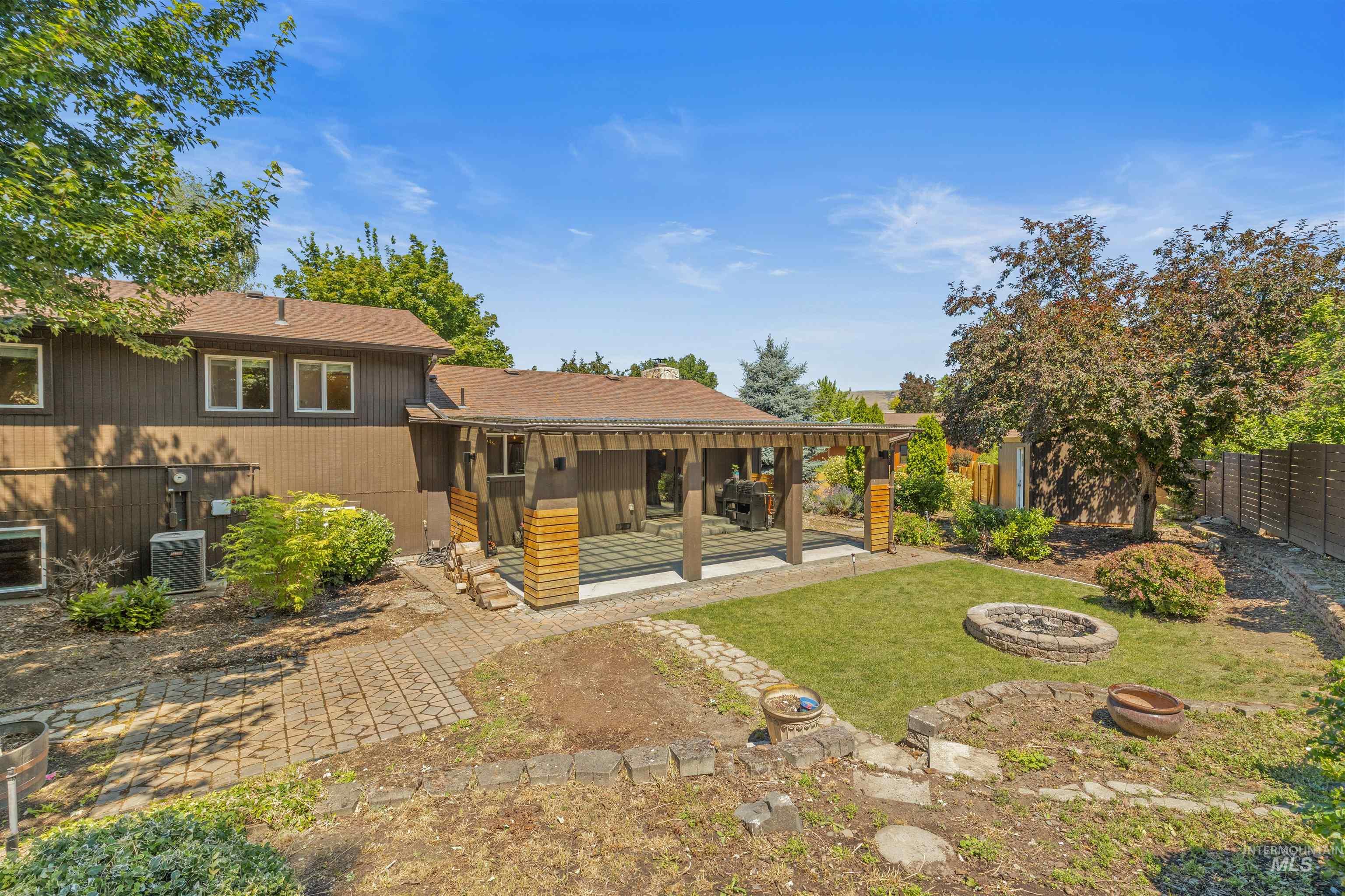 Rear exterior featuring a covered patio with wood columns, a manicured lawn area, and a stone fire pit