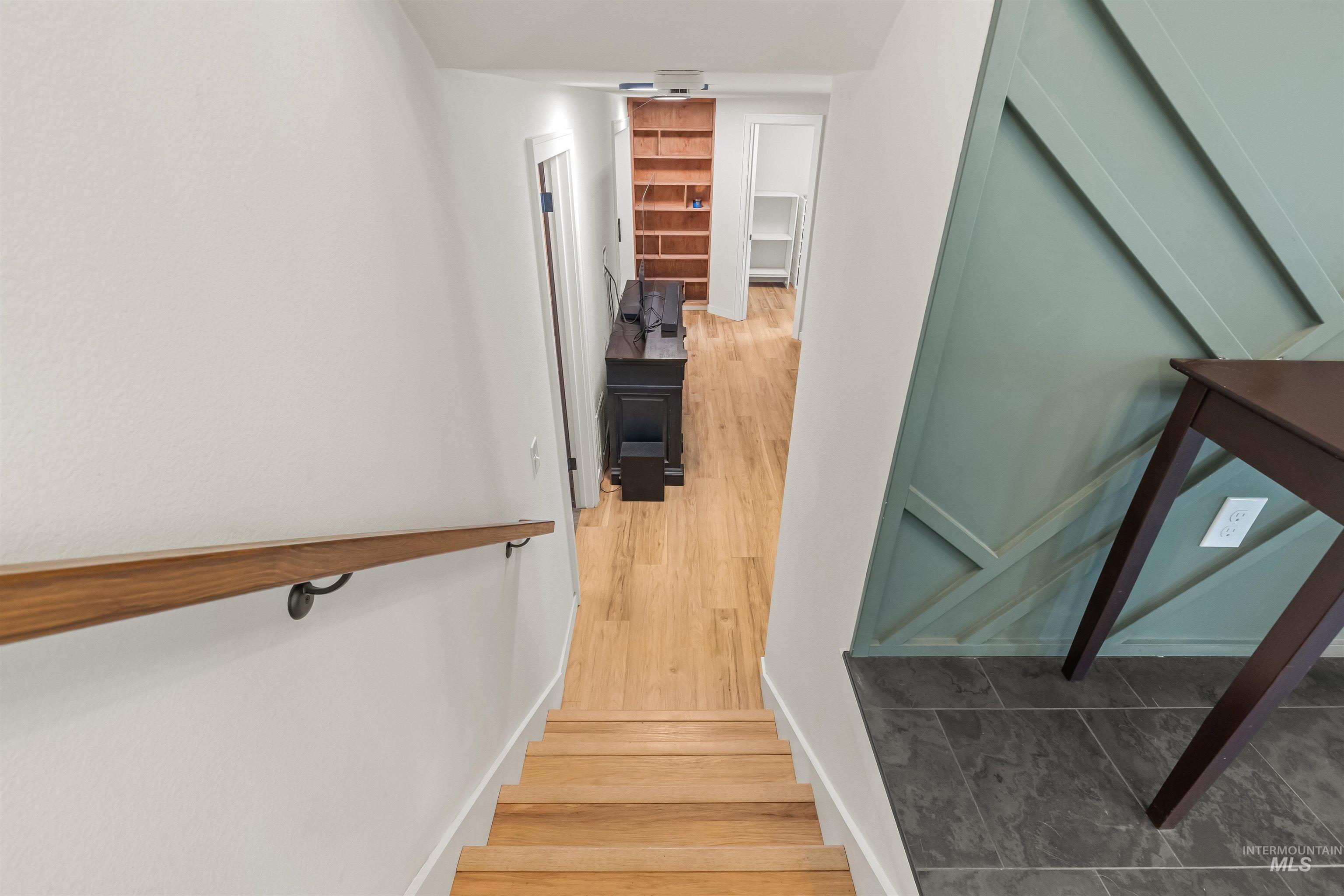 Staircase featuring wood steps and a wood handrail, leading to a hallway with wood-finish flooring
