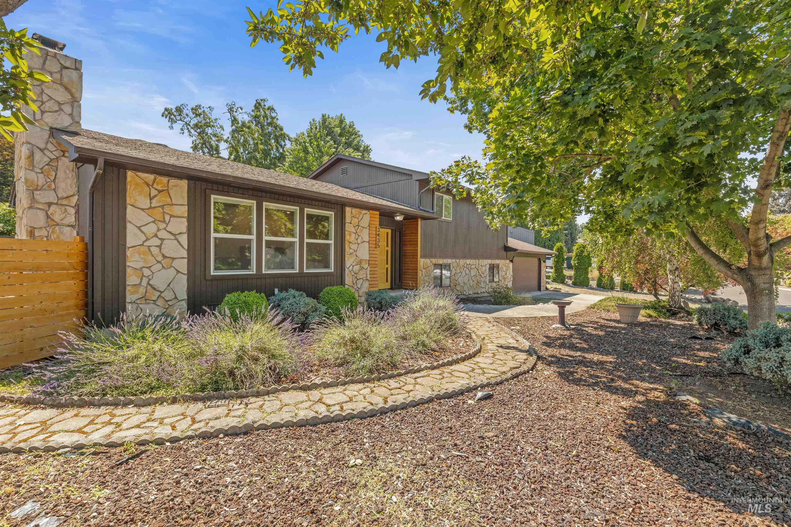 Stone and wood-sided exterior featuring multiple window banks, an integrated stone chimney, and a natural wood fence