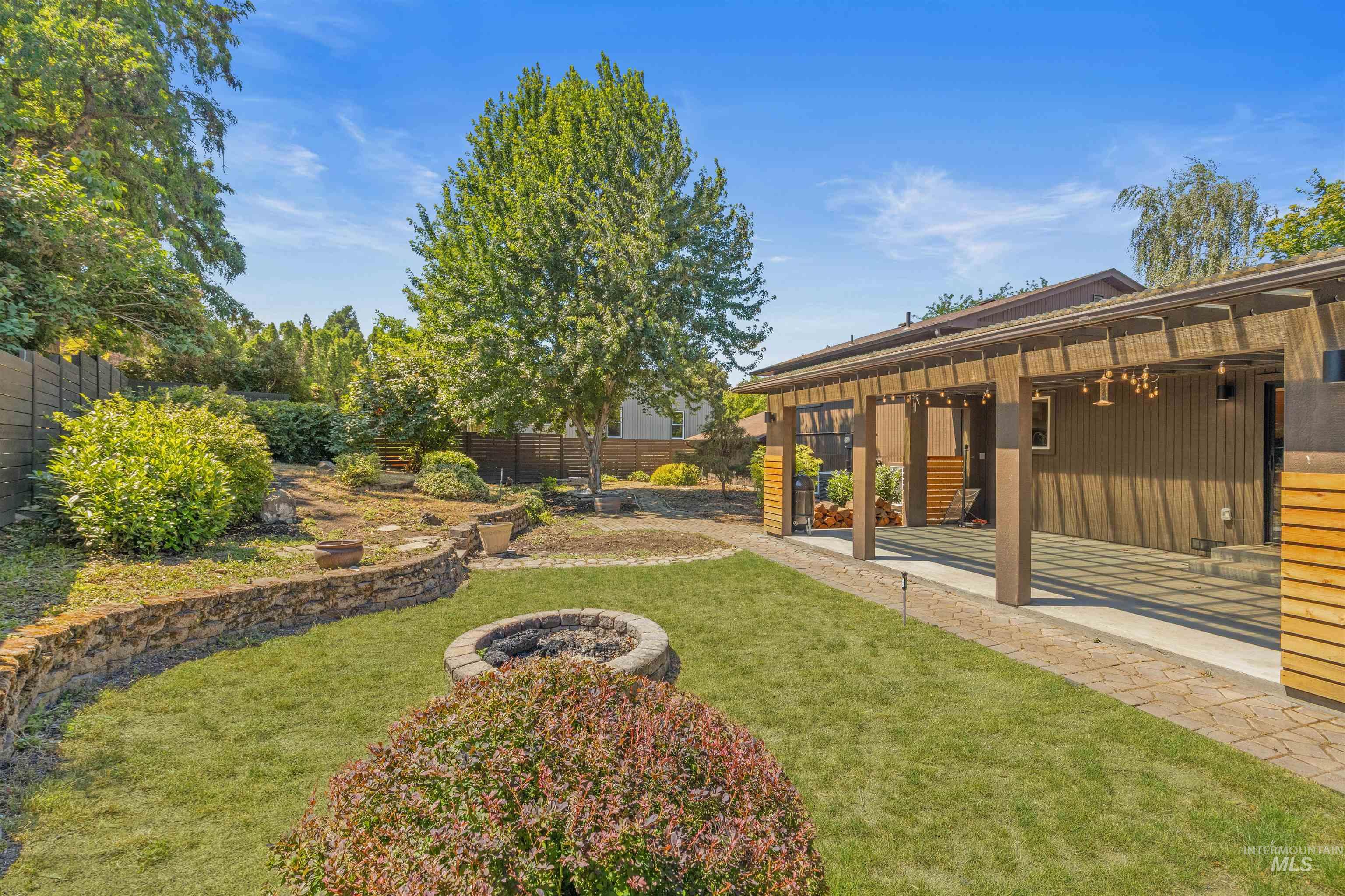 Expansive backyard featuring a stone-clad fire pit, mature landscaping, and a wood-slat privacy fence