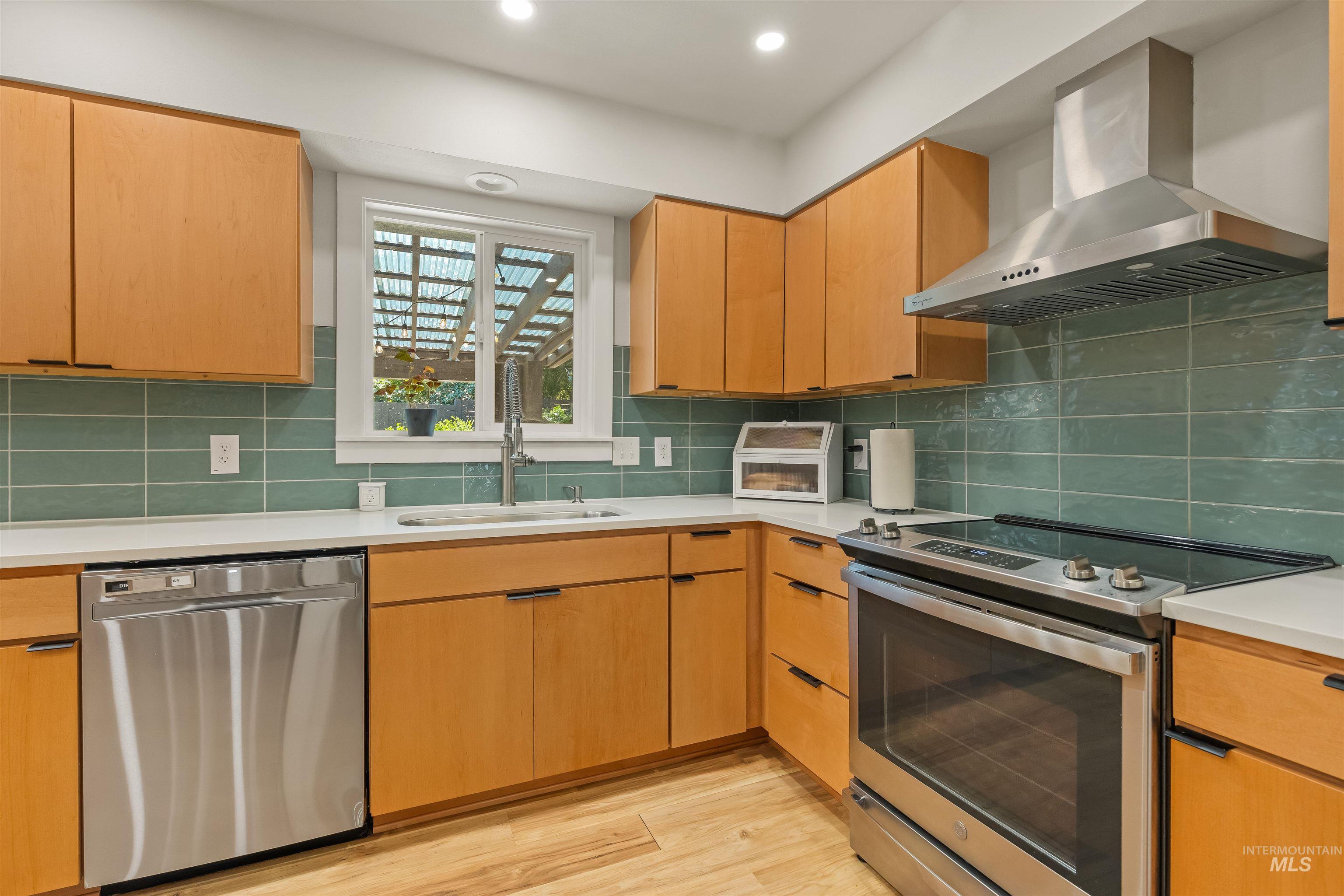 Kitchen featuring wood-finish cabinetry, stainless steel appliances, white countertops, and a green subway tile backsplash