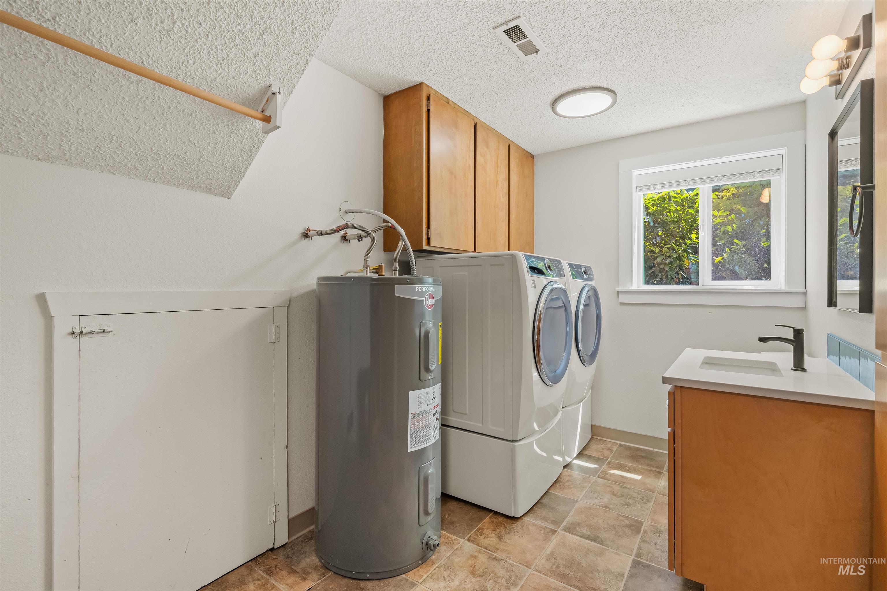 Dedicated laundry area featuring a built-in wood cabinetry, a water heater, and durable tile flooring