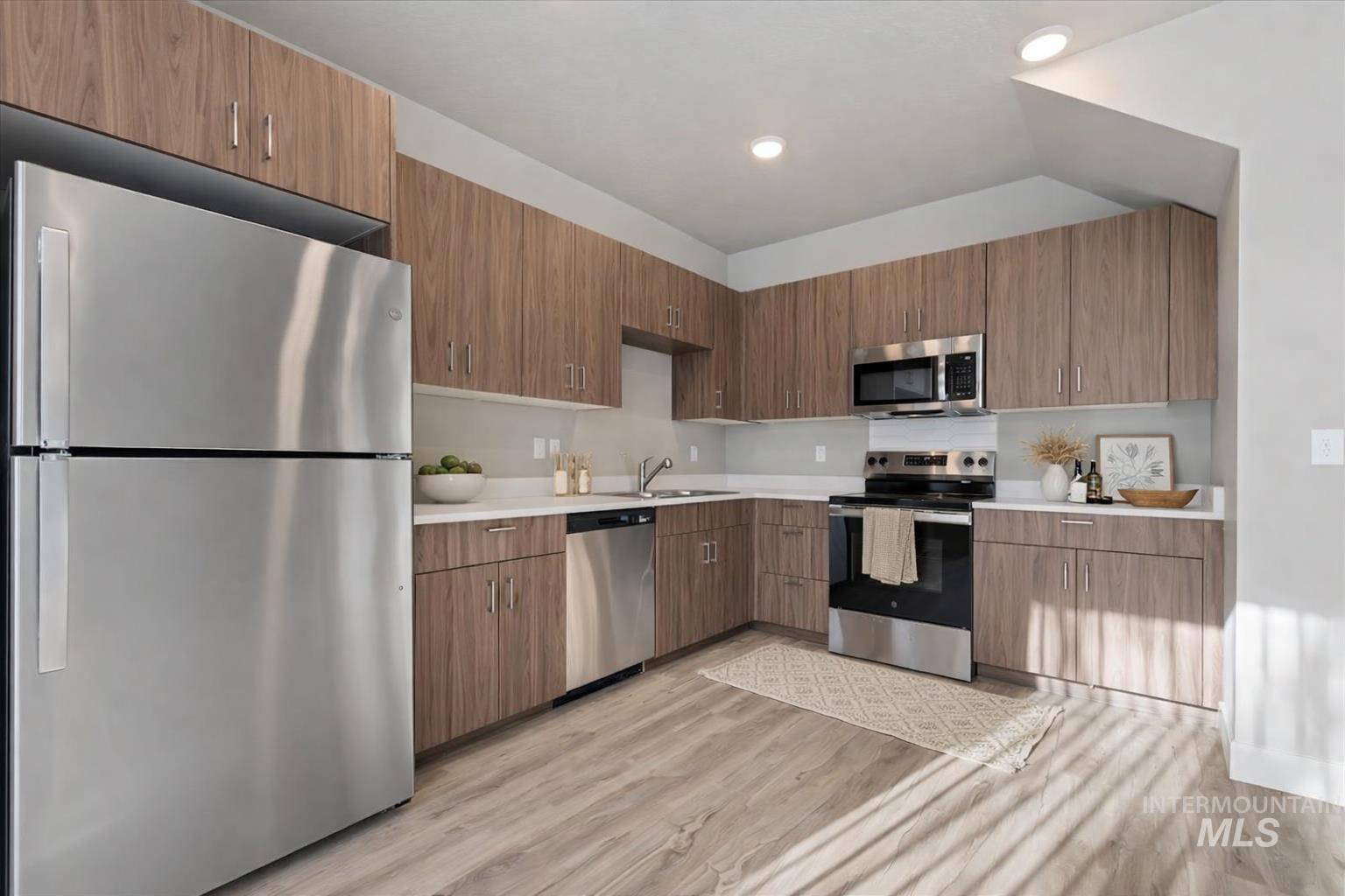 Kitchen featuring appliances with stainless steel finishes, light countertops, light wood-type flooring, modern cabinets, and recessed lighting