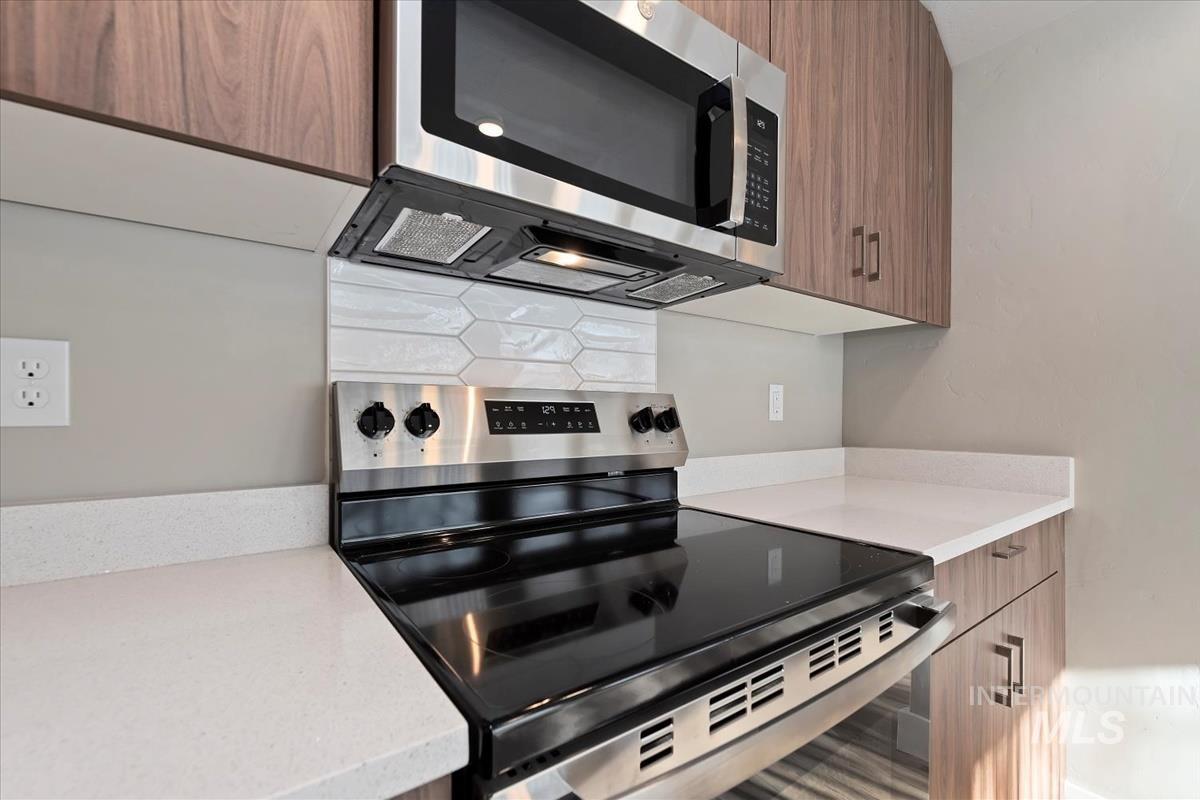 Kitchen with stainless steel appliances, brown cabinets, modern cabinets, light stone countertops, and tasteful backsplash
