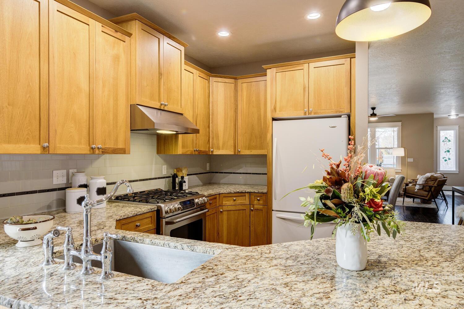 Kitchen featuring freestanding refrigerator, gas range, decorative backsplash, under cabinet range hood, and light stone countertops