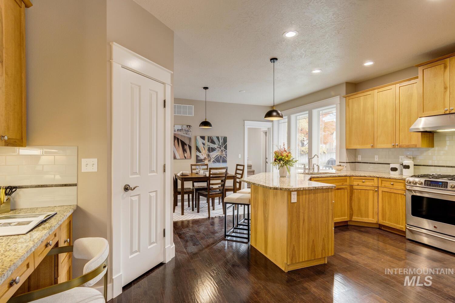 Kitchen featuring backsplash, gas stove, light stone countertops, a kitchen bar, and dark wood finished floors