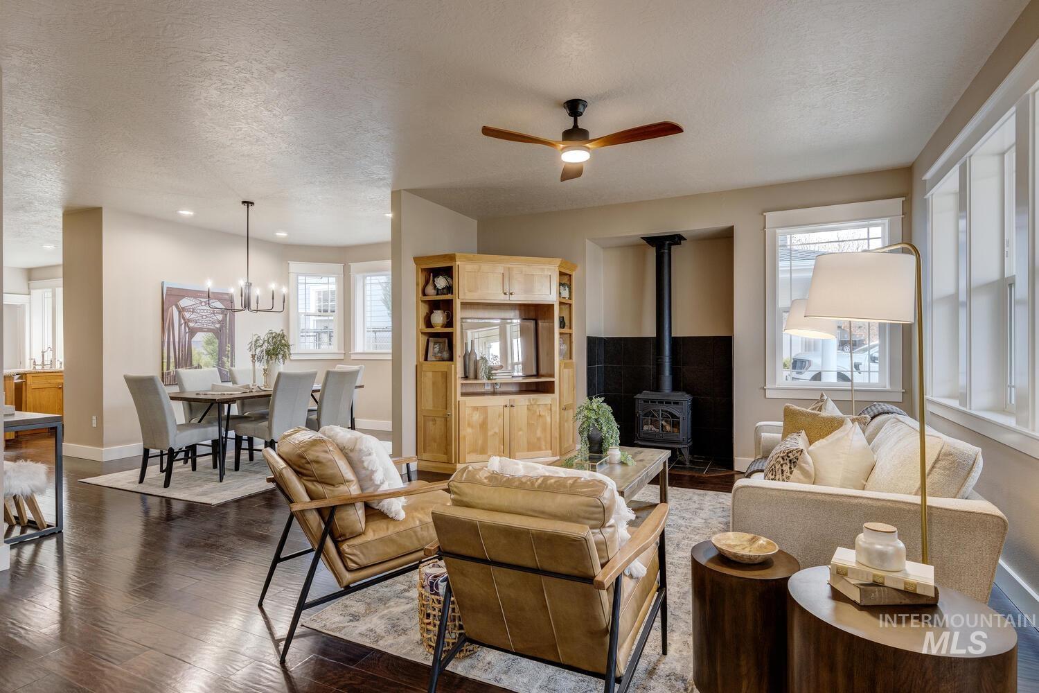 Living area with a wood stove, a textured ceiling, dark wood finished floors, ceiling fan, and a chandelier