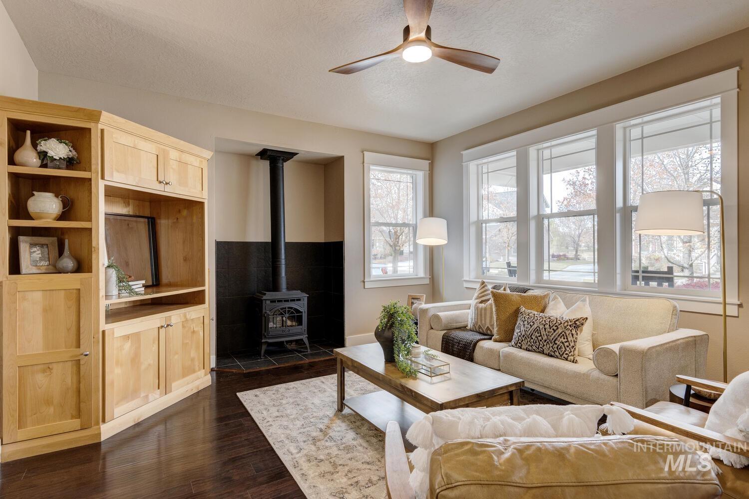 Living area featuring a wood stove, dark wood finished floors, a textured ceiling, and ceiling fan