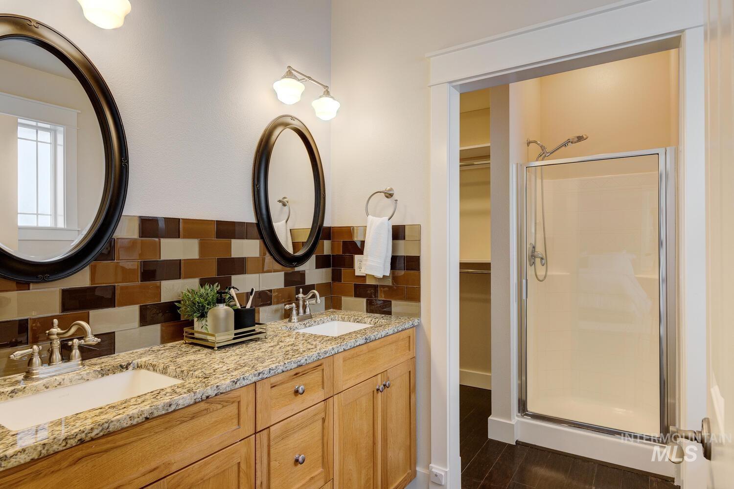 Full bath with double vanity, tasteful backsplash, a stall shower, and a walk in closet